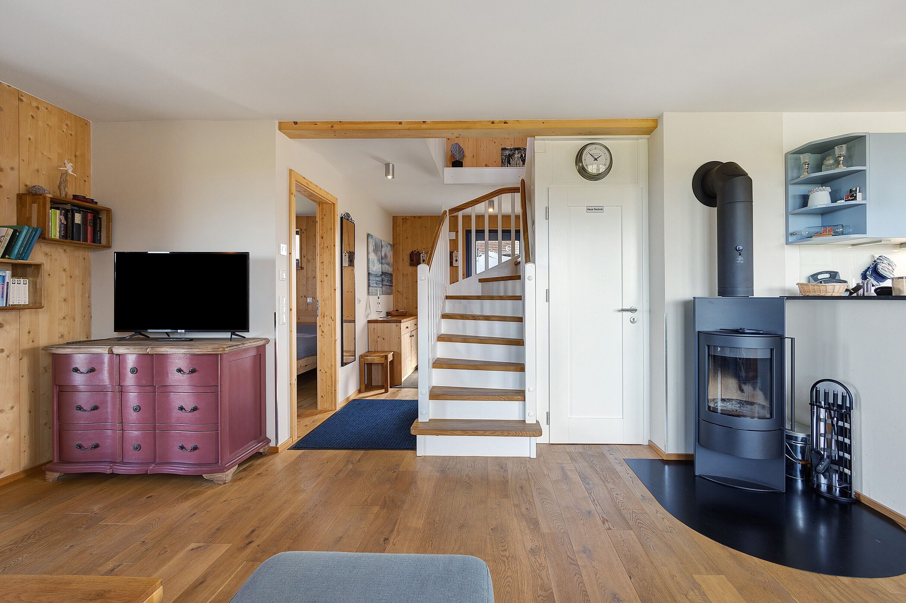 Ein gemütliches Wohnzimmer mit einer Holztreppe, einem Fernseher, einem pinken Schrank und einem Kamin.