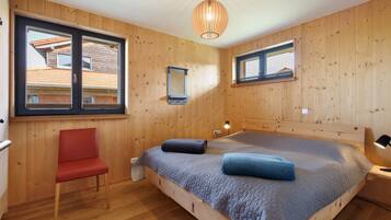 A wooden-paneled bedroom with a bed, a chair, a window, and a hanging light fixture.
