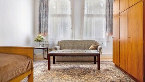 A bedroom with a bed, a sofa, a wooden wardrobe, and a window with curtains.