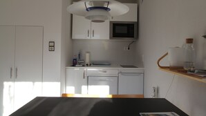 A compact kitchen with white cabinets, a microwave, a dishwasher, and a wooden shelf with a glass jar. - Studio Apartment 'Gartenstudio Peony' with Mountain View, Private Terrace and Wi-Fi (Birgitz)