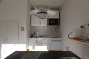 A compact kitchen with white cabinets, a microwave, a dishwasher, and a wooden shelf with a glass jar.