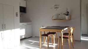 A kitchen with white cabinets, a microwave, a wooden dining table with chairs, and a hanging light fixture. - Studio Apartment 'Gartenstudio Peony' with Mountain View, Private Terrace and Wi-Fi (Birgitz)