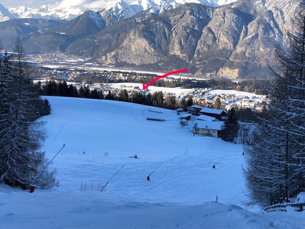 A snow-covered ski slope with a town in the background, a ski lift, and mountains.