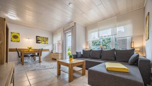 Ein Wohnzimmer mit einer Couch, einem Couchtisch, einem Esstisch mit Stühlen und einer Küchenzeile.