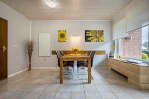 A dining area with a wooden table, black chairs, and a vase of yellow flowers. There are two sunflower paintings on the wall.