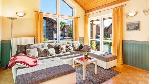 Ein gemütliches Wohnzimmer mit einer Eckcouch, einem kleinen Tisch und einem Fenster mit Vorhängen.
