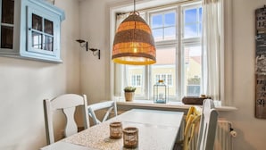 A dining area with a table, chairs, a hanging light fixture, a window with curtains, and a blue cabinet. - "Marisol" - 700m from the sea by Interhome (Skagen)