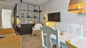 A modern living room with a sofa, a dining table with chairs, a TV mounted on the wall, and a wicker lamp. - "Marisol" - 700m from the sea by Interhome (Skagen)