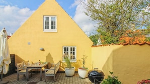 A yellow house with a triangular roof, a patio with a table and chairs, and potted plants. - "Marisol" - 700m from the sea by Interhome (Skagen)