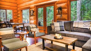 L’intérieur d’une cabane en rondins comprend un coin repas, des sièges et de grandes fenêtres donnant sur la forêt.