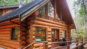 Une cabane en rondins dotée d’une terrasse, de grandes fenêtres et d’une cheminée.