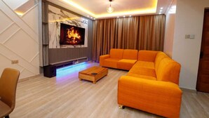 A modern living room with a sectional sofa, a flat-screen TV, and a fireplace. - Lux Suites Nakuru VIP Suites (Nakuru)
