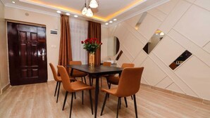 A dining area with a rectangular table, six chairs, a vase with red flowers, and a large mirror on the wall. - Lux Suites Nakuru VIP Suites (Nakuru)