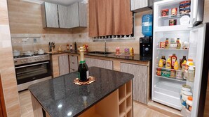 A modern kitchen with a granite countertop, stainless steel appliances, and a built-in refrigerator stocked with various food items. - Lux Suites Nakuru VIP Suites (Nakuru)