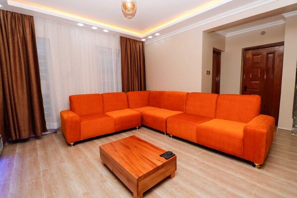 Una sala de estar moderna con un amplio sofá modular naranja, una mesa de centro de madera y un gran ventanal con cortinas.
