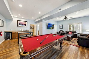 A pool table in a room with a fireplace, a sofa, and a ceiling fan. - HUGE 7Br (+Bonus Room) Cabin, Pool Table, Games (South Lake Tahoe)