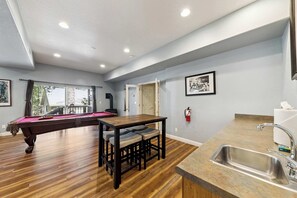 Une pièce comprenant une table de billard, une table à manger avec des chaises, un coin cuisine avec un évier et un extincteur fixé au mur.
