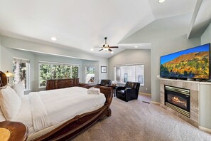 A bedroom with a large bed, a fireplace, a television, and a view of trees through the windows. - HUGE 7Br (+Bonus Room) Cabin, Pool Table, Games (South Lake Tahoe)
