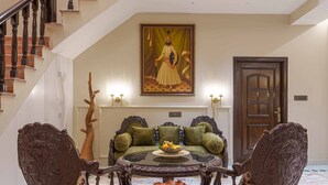 Una gran escalera con barandilla de madera, un cuadro grande en la parte superior de la escalera, y un área de descanso con sillas ornamentadas y una mesa.