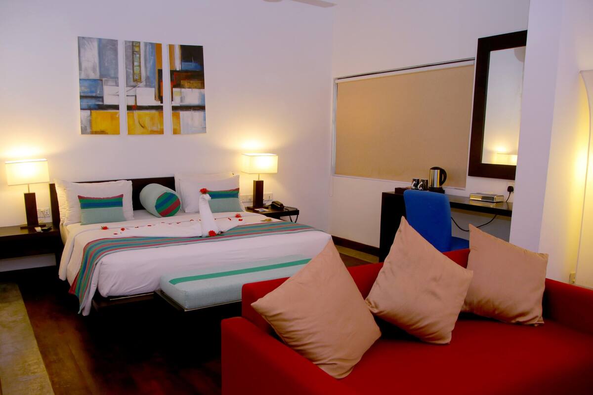 A hotel room with a bed, a red sofa, a desk, and a large mirror.