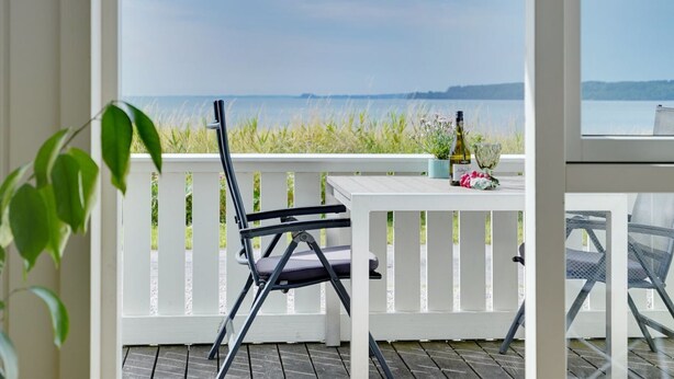 A balcony with a white railing, a folding chair, a table, a bottle of wine, and a vase with flowers. - "Liutulf" - 40m from the sea by Interhome (Haderslev)