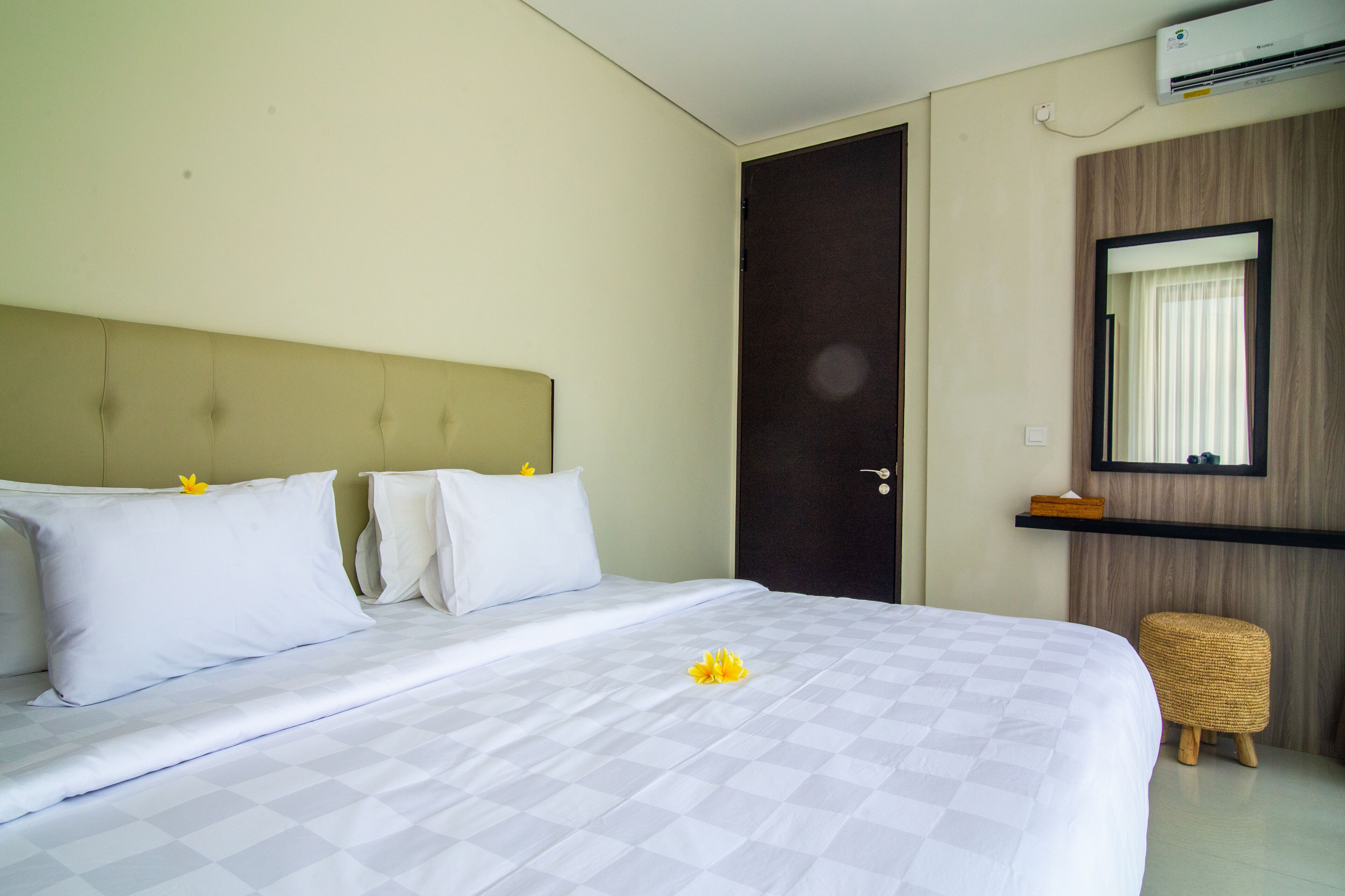 Une chambre d’hôtel avec un lit, une porte en bois, un petit tabouret et un miroir au mur.