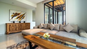 Un soggiorno moderno con un divano componibile, un tavolino da caffè in vetro con fiori, un mobile contenitore in legno e un grande quadro astratto appeso alla parete.