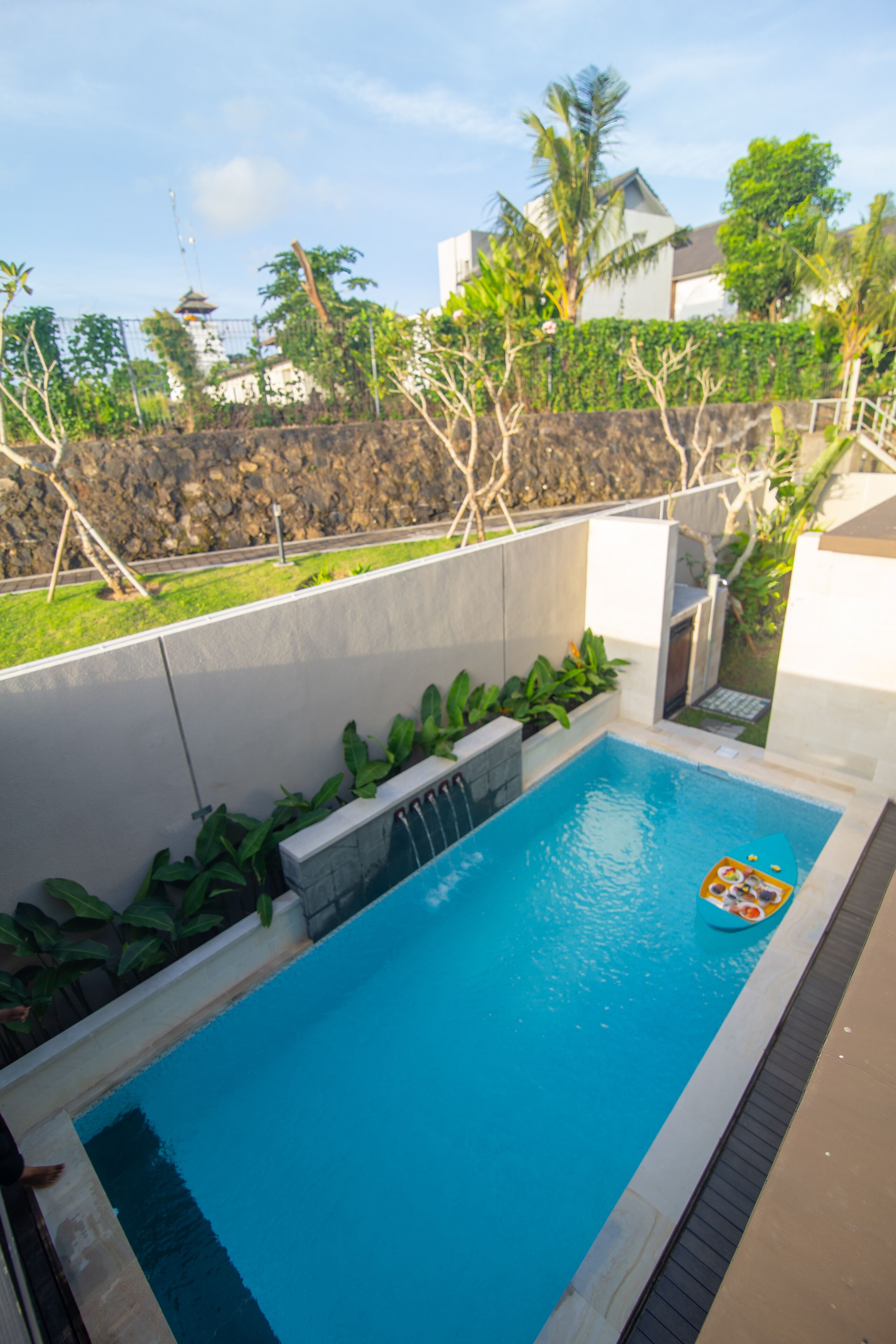 Una piscina con un pequeño bote inflable, rodeada por un muro de piedra y vegetación.