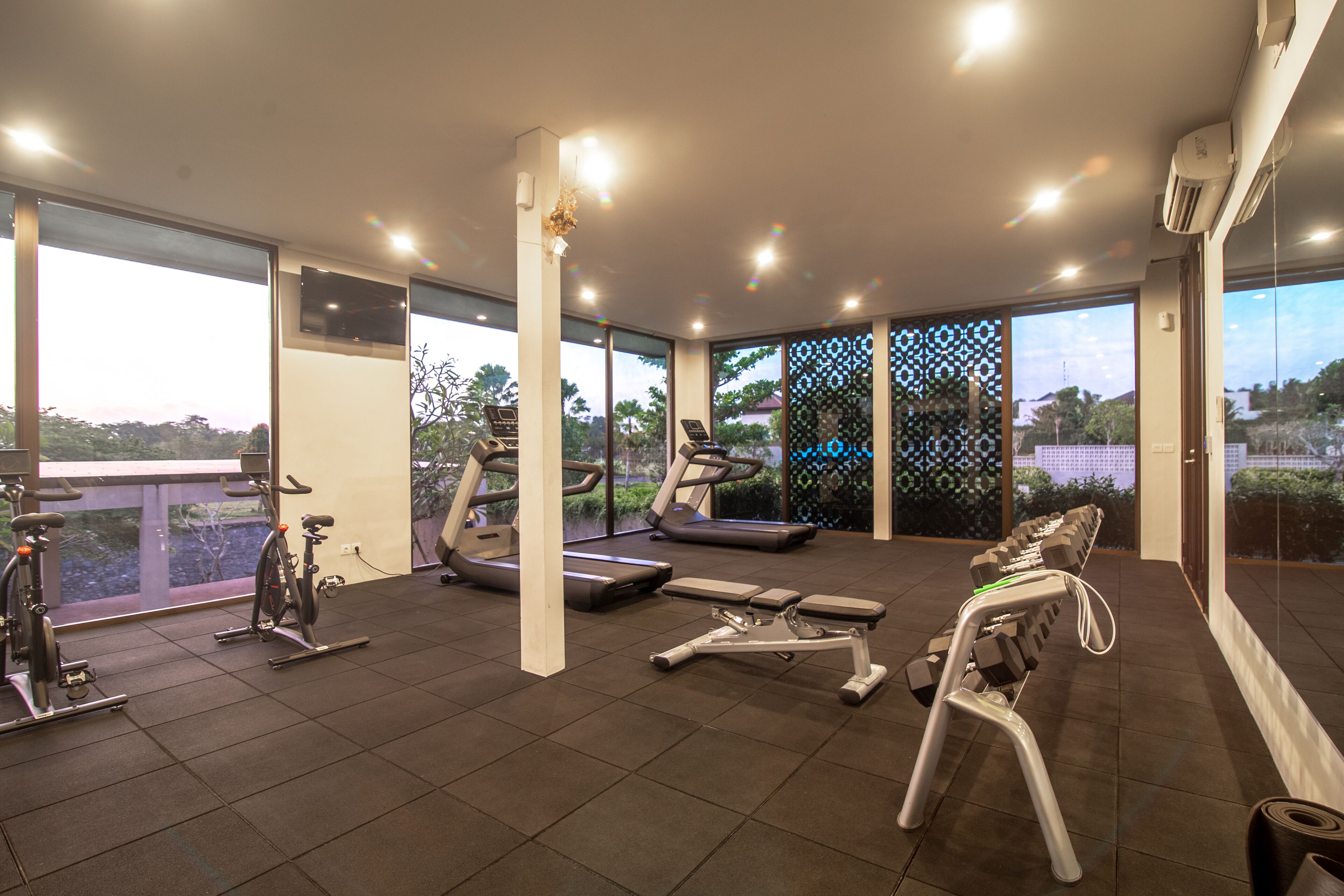 Een sportschool met trainingsapparatuur, grote ramen en uitzicht op groen.