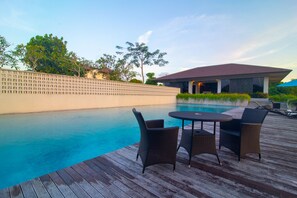 A swimming pool with a wooden deck, two wicker chairs, and a covered area with a red roof. - Tridi Beach Villa by Nagisa Bali (Tabanan)