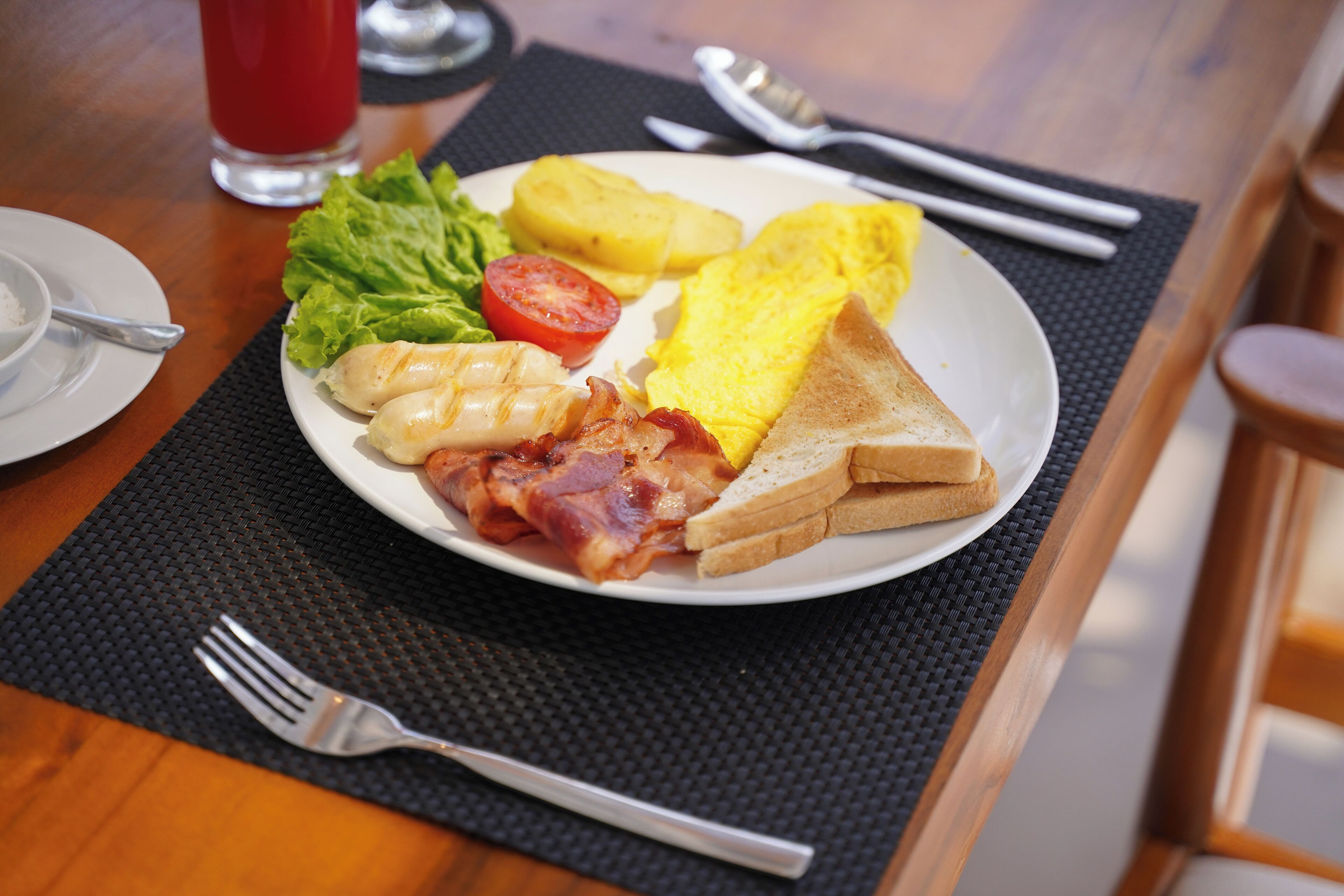 A breakfast plate with eggs, bacon, toast, and vegetables on a table.