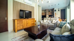 Un soggiorno moderno con un mobile in legno, una TV a schermo piatto, un tavolino da caffè scuro e un divano beige con cuscini decorati.
