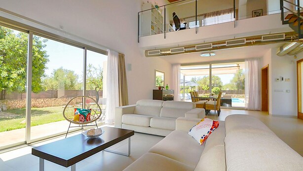 A spacious living room with a large white sofa, a coffee table, and a dining area with chairs. There is a balcony with a railing and a view of the outdoors. - Vacation home Caleu by Interhome (Binissalem)