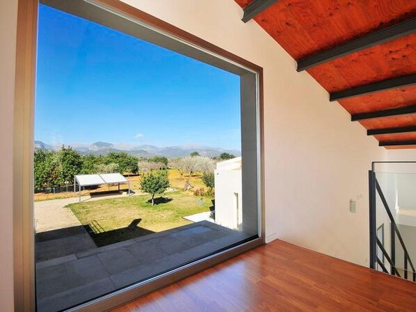 Una habitación moderna con un gran ventanal corredero que da a un balcón con vistas a viñedos y montañas.