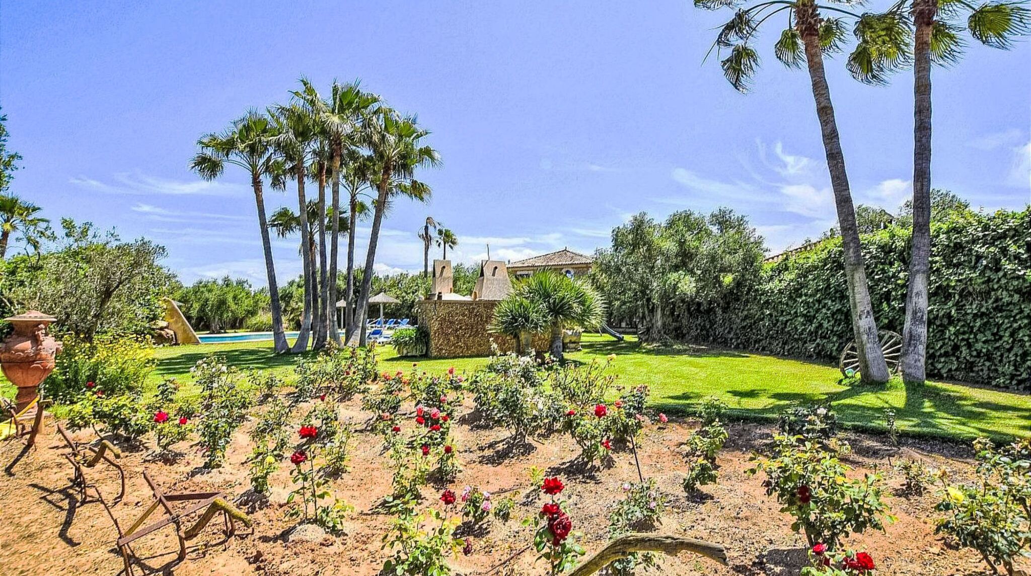 Un jardín con palmeras, una piscina y una casa con techo de tejas.