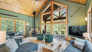 A spacious living room with a high ceiling, large windows, and a fireplace. - 4000sqft, 1-acre Custom Cabin Retreat w Game Room, Hot Tub & Sauna @Mt Hood (Rhododendron)