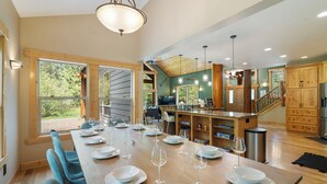 A spacious kitchen with a long dining table set for six, wooden cabinets, and a view of the outdoors. - 4000sqft, 1-acre Custom Cabin Retreat w Game Room, Hot Tub & Sauna @Mt Hood (Rhododendron)