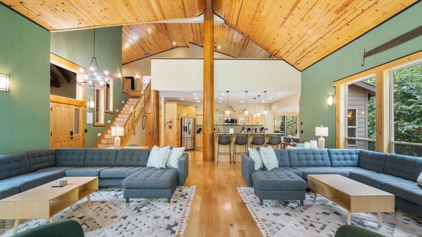 A spacious living area with a high wooden ceiling, a kitchen in the background, and a staircase leading to an upper level. - 4000sqft, 1-acre Custom Cabin Retreat w Game Room, Hot Tub & Sauna @Mt Hood (Rhododendron)