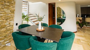 A spacious dining area with a high ceiling, a staircase leading to an upper level, and a view of the outdoor area. - Luxury Duplex, Poblado Gem!
 (Medellín)