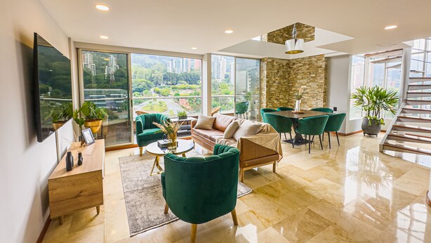 A spacious living room with a large window, a dining area, and a staircase. - Luxury Duplex, Poblado Gem!
 (Medellín)