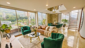 A spacious living room with a sofa, two green armchairs, a coffee table, and a dining area with a table and chairs. - Luxury Duplex, Poblado Gem!
 (Medellín)