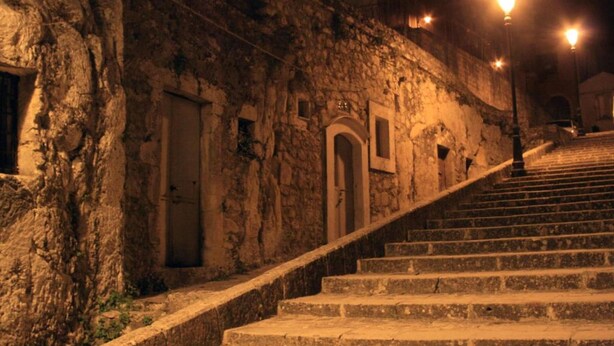 Una escalera de piedra que sube hacia un edificio con arcos y una pared de piedra.