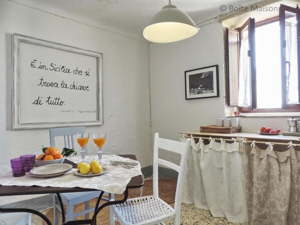 A dining area with a table set for two, a framed quote on the wall, and a window with curtains.