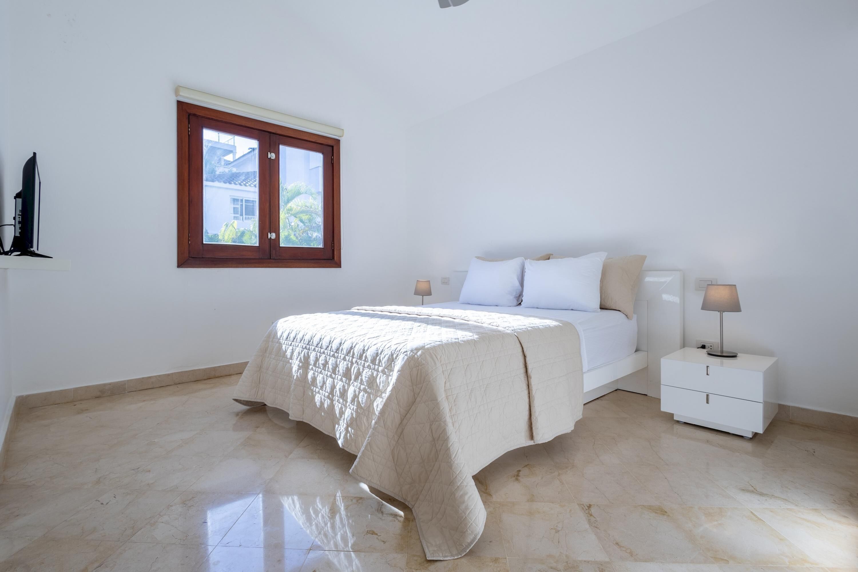 A bedroom with a bed, nightstands, a window, and a lamp.