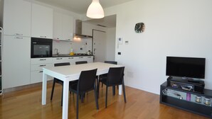 A modern kitchen with white cabinets, a dining table with chairs, a black TV stand, and a hanging light fixture. - La Castellana Relax in Sirmione (Sirmione)