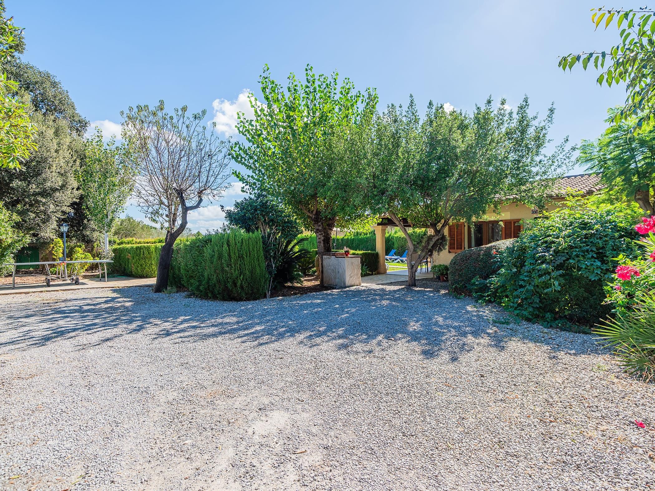 A gravel driveway leading to a building with a pergola and a chair.