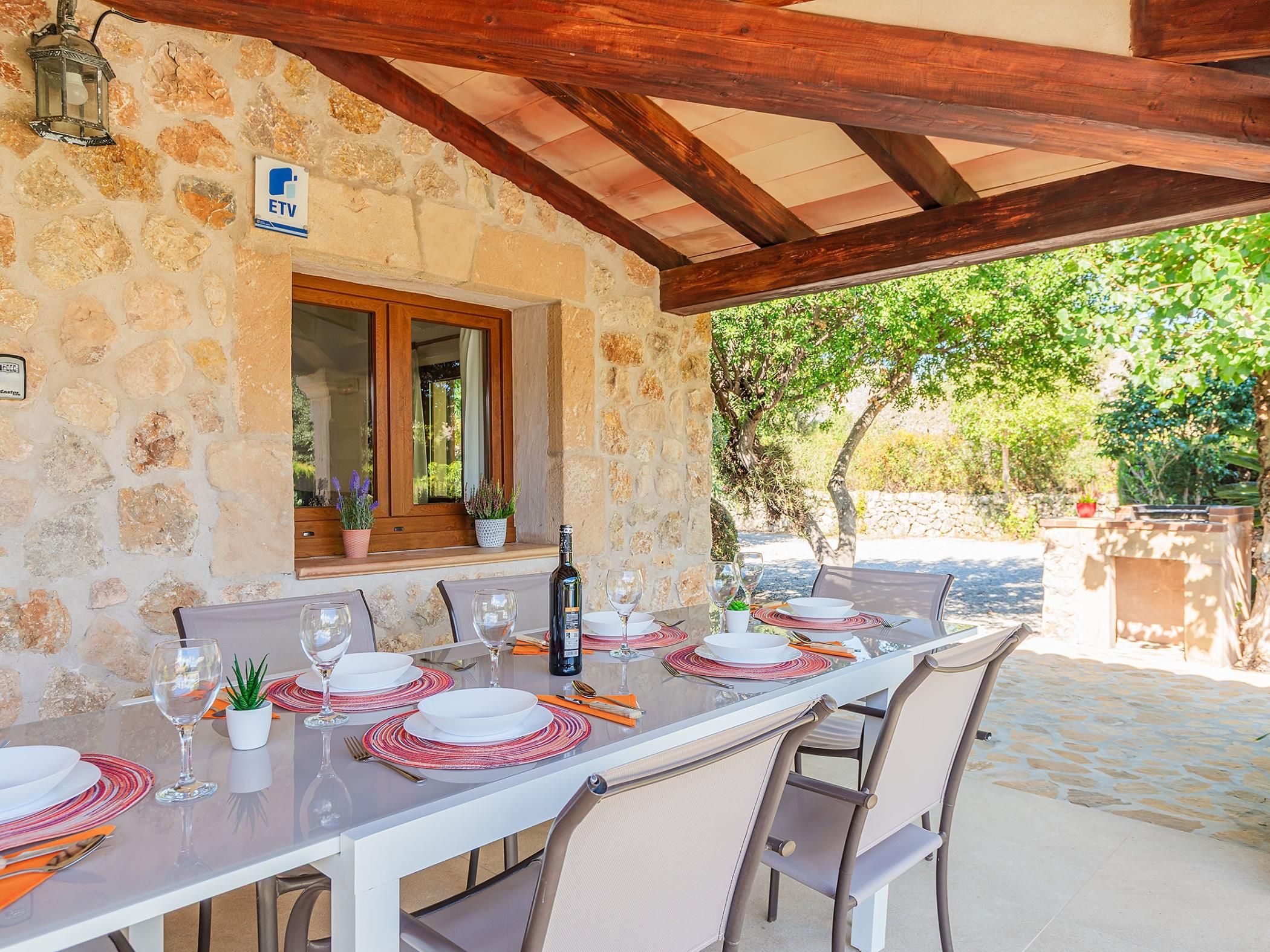 An outdoor dining area with a stone wall, wooden beams, and a view of greenery.