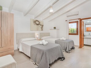 A hotel room with two beds, a wardrobe, a painting, a bedside table with a lamp, and a window with a view.