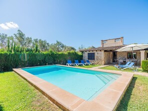 A rectangular swimming pool with a stone border, surrounded by a well-maintained lawn and a stone building with a tiled roof.