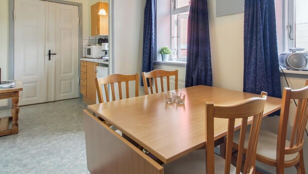 Un coin repas avec une table et des chaises en bois, une cuisine à l’arrière-plan et une fenêtre avec des rideaux.